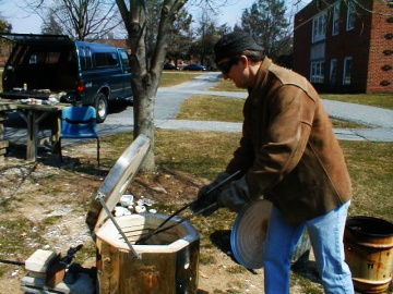 Milt Friedly pulls pottery from kiln with tongs.