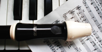 A wooden recorder sits on a sheet of music, with piano keys in the background